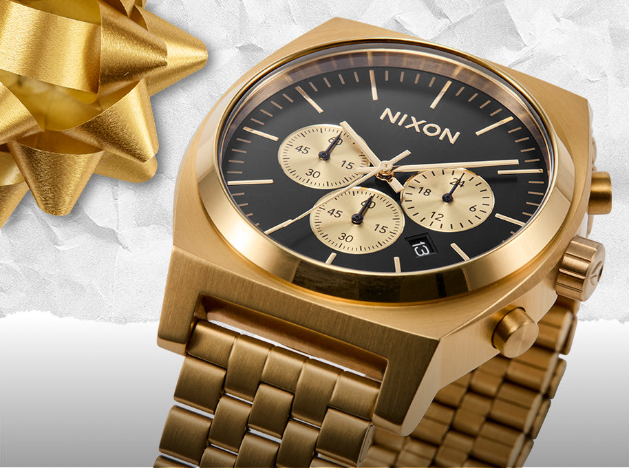Gold Nixon Time Teller Chrono watch with black face on a textured white background